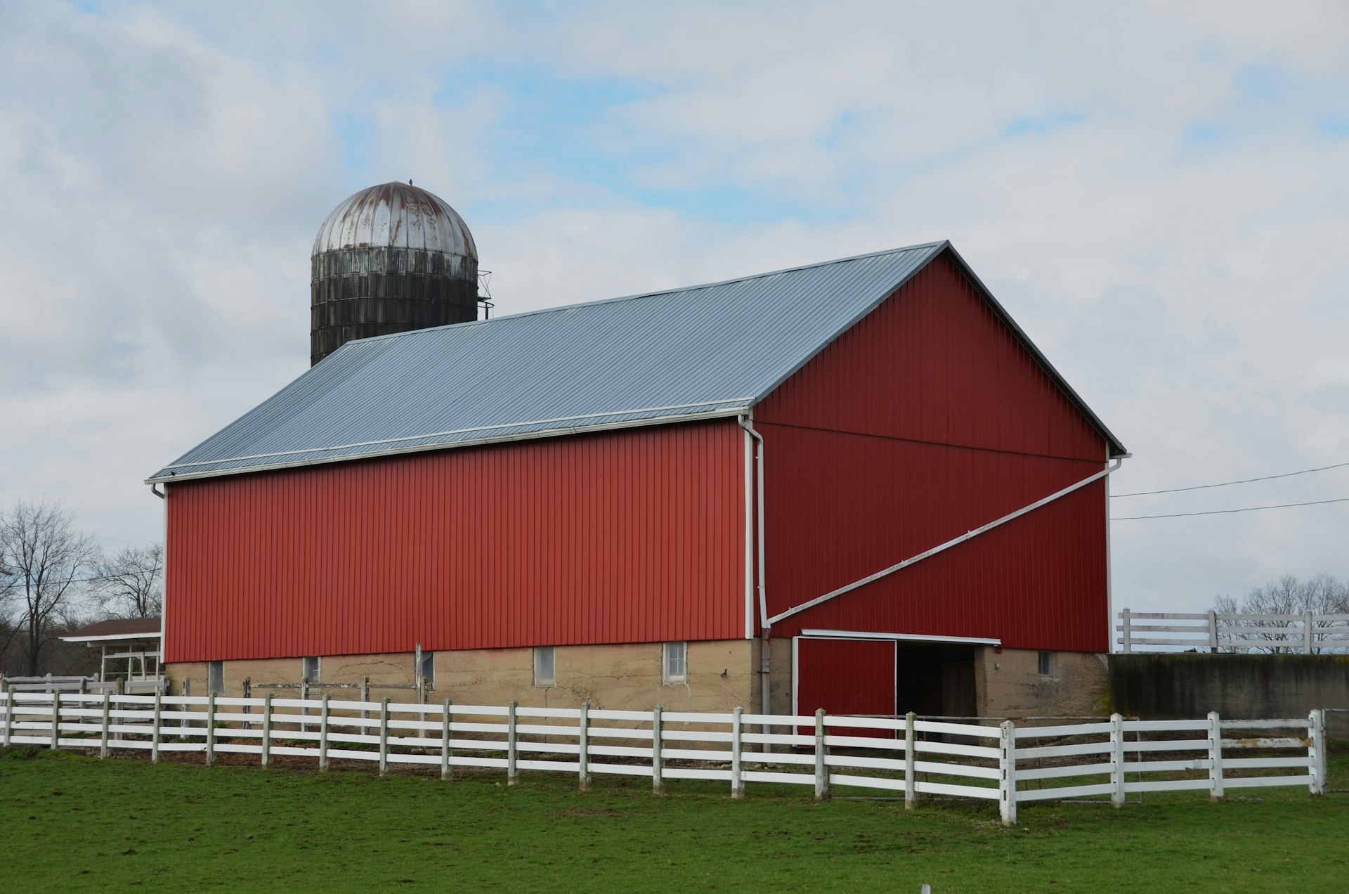 A red barn with a white fence in green fields under a blue sky